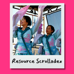 two women of Chinese heritage, with dark hair and brown eyes, wearing traditional Chinese dancing blue dresses with long flowing pink sleeves. They are smiling as they dance with their hands in the air.