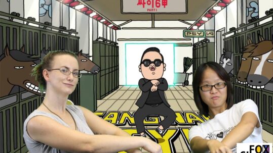 Christina Berkshire (Left) is a Caucasian woman wearing a light grey tank top and glasses. She has brown hair that is up in a pony tail. Fox Si-Long Chen (right) is of Taiwanese descent, is wearing a white tshirt and black framed glasses. She has short dark hair parted down the middle. Both women are standing in front of a green screen with gangnam style cartoon playing on it. Both girls are dancing with the character.