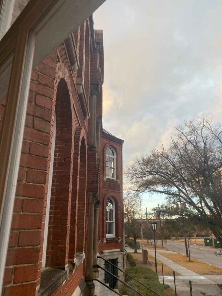 Photo of the facade of Sacred Heart as seen from Brendas window. it is a red brick catholic church with renaissance style arches and stained glass.
