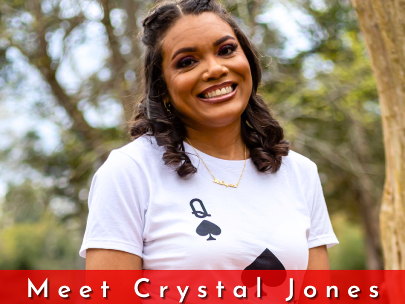Crystal Jones is a woman with brown curly hair. She is waring a queen of spades tshirt and smiling.
