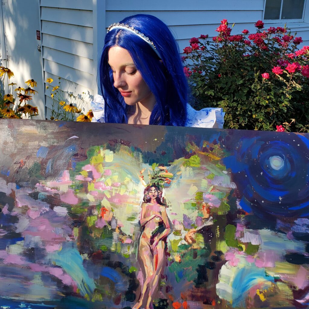 Lexi Kay White standing with her paiting. She is a Caucasian woman. She is wearing a blue, long haired wig with a silver crown and white dress. She is holding an acrylic painting of a woman surrounded by flowers.