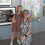 Photo of Lillie Morris and her grandaughter Valley. Lillie is a Caucasian woman with gray hair and black glasses. She is wearing a black and white spotted dress. Valley is a 9 year old girl. She is wearing a brown dress and white sneakers. She is Caucasian with long brown hair.