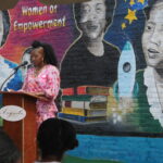 Salonika Rhyne, mural artist, giving a speech. She is an African-American woman with a bright pink dress and poofy hair.