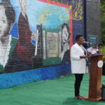 Photo of African-American woman in white suit jacket and black pants giving a speech