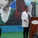 Photo of African-American woman in white suit and black pants giving a speech