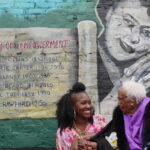 Salonika Rhyne and Ruth B. Crawford smiling in front of the mural