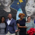 Group photo including Corey Rogers and Pax Bobrow in front of the mural