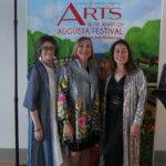 Photo of three Caucasian woman standing in front of a backdrop posing together.
