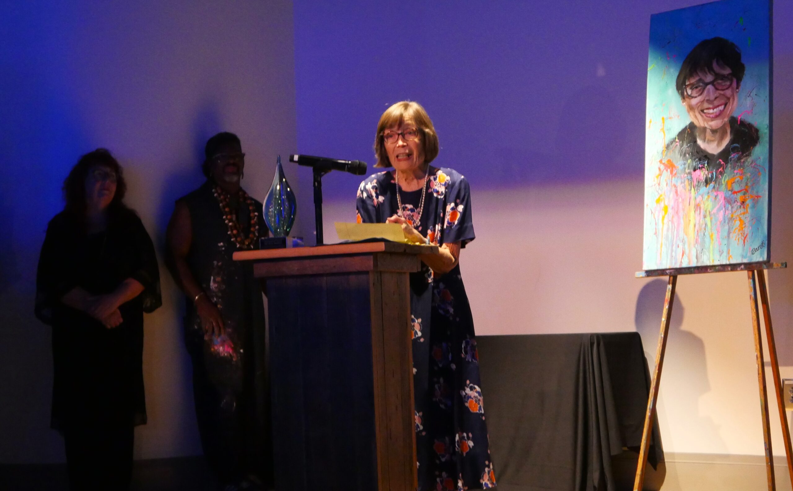 Older Caucasian woman with short brown hair receiving an award, giving a speech behind a podium.