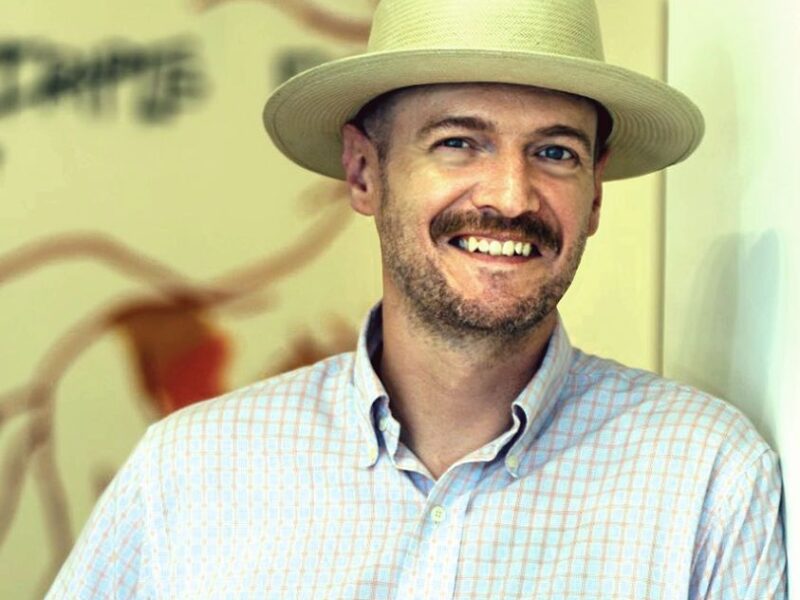 Matt Porter is a Caucasian man with a brown beard and mustache. He is wearing a white, wide brimmed hat with a blue button down shirt.