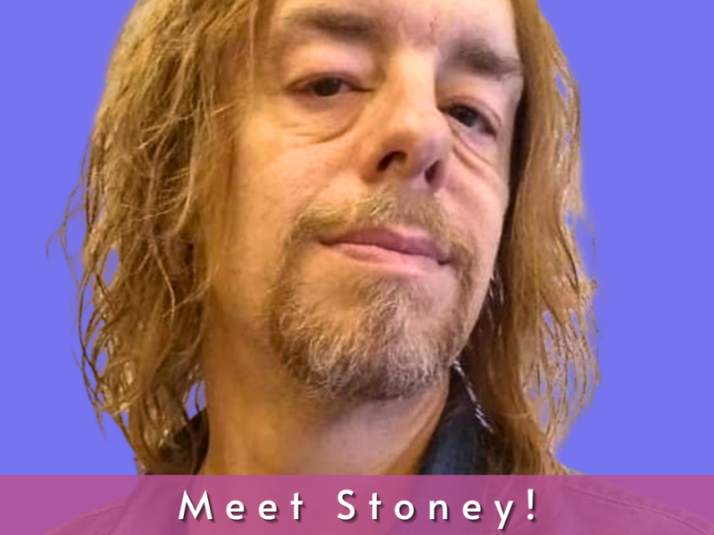 John "Stoney" Cannon is a Caucasian male with sandy brown hair to his shoulders. He has brown eyes and is wearing a denim button down shirt.