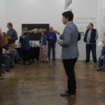 Man giving an artist talk. He is wearinga grey suit jacket.