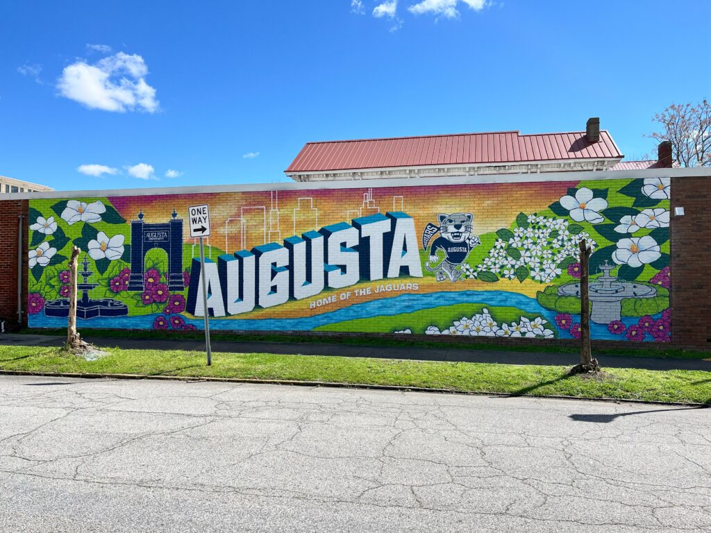 colorful mural that says "augusta" with flowers and the river on a brick wall