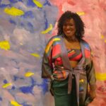 A nicely dressed African American woman posing in front of a painted backdrop