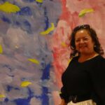 A Hispanic woman posing in front of a painted backdrop