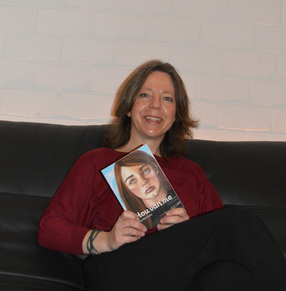 Caucasian woman posing with a book. She is wearing a red sweater and has short brown hair.