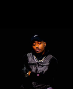 an African American man wearing a black baseball hat and denim vested hoodie.